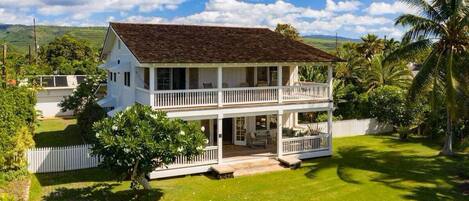 A two-story house with a balcony, surrounded by a well-maintained lawn and palm trees.