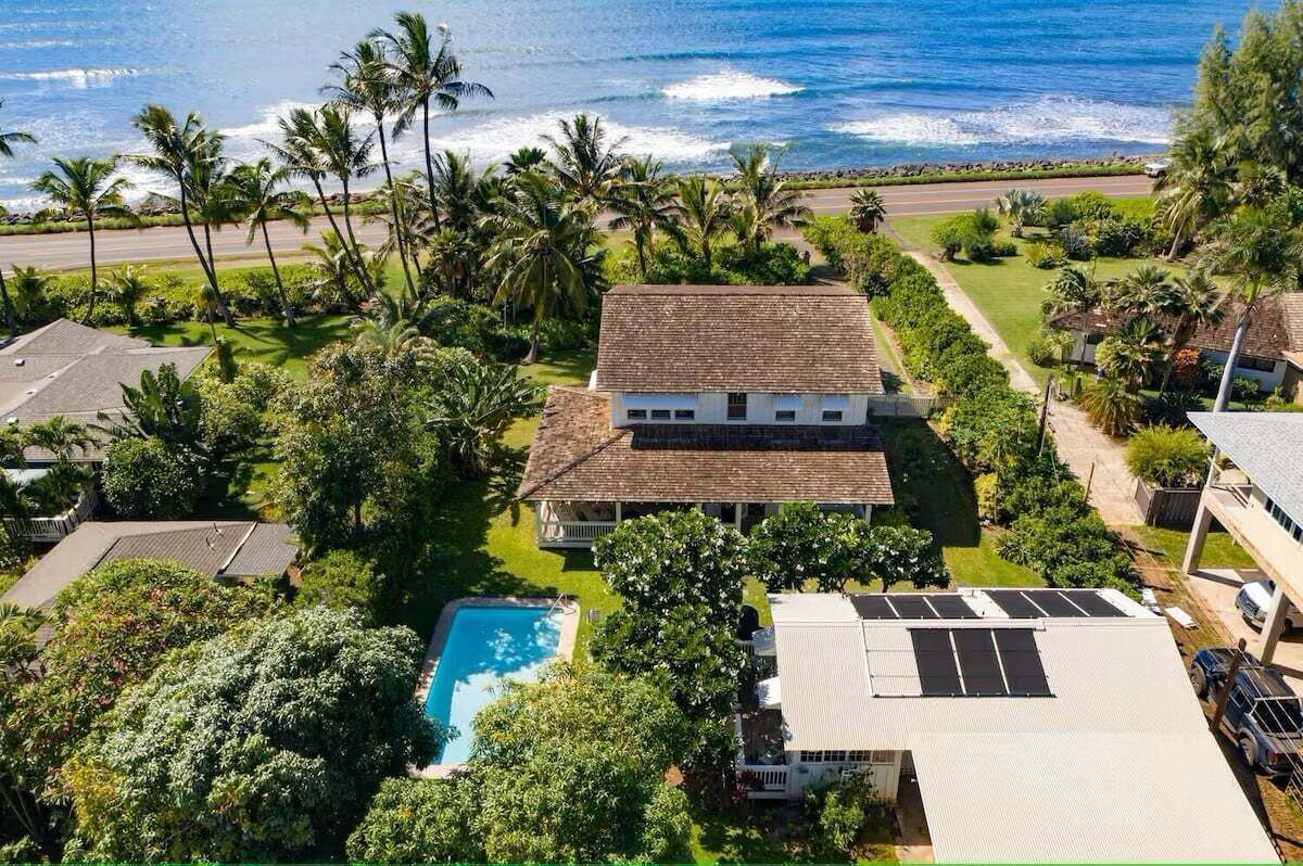 A house with a swimming pool, surrounded by palm trees and a view of the ocean.