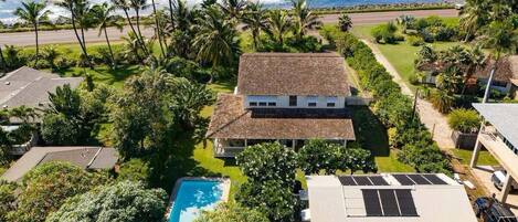A house with a swimming pool, surrounded by palm trees and a view of the ocean.