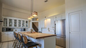 Une cuisine moderne avec des meubles blancs, un îlot central doté de tabourets de bar, des appareils en acier inoxydable et des luminaires suspendus.