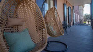 Un balcon avec deux fauteuils suspendus en osier, une table et une vue sur la rue.