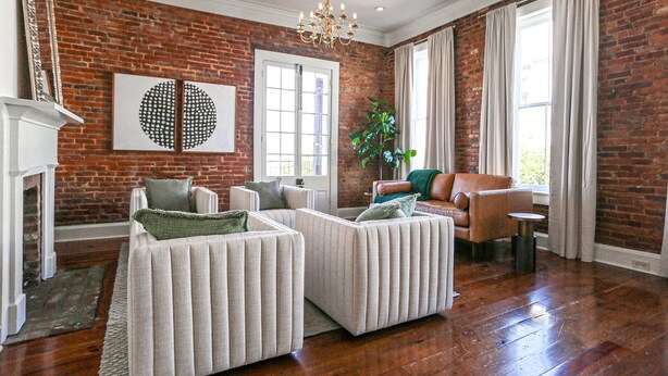 Un salon avec un mur en briques, deux canapés blancs recouverts de tissu, une plante verte et une cheminée.