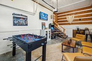 A room with a foosball table, a GameRoom sign, a staircase, and a bar area.