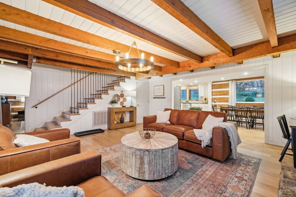 A spacious living area with a wooden ceiling, a round coffee table, leather sofas, and a staircase leading to another level.