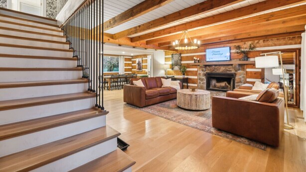 Amplia sala de estar con escalera de madera, sofás de cuero, chimenea y televisión.