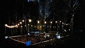 An outdoor area with string lights, tables, and chairs arranged for an event.