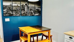 A dining area with a wooden table and benches, a cityscape mural on the wall, and a hanging light fixture.
