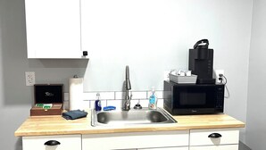 A kitchen with a sink, a microwave, and a coffee maker. There is a cabinet with a small television on top.