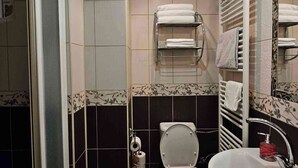 Et badeværelse med toilet, håndvask og bruseniche. Der er håndklæder på en holder og en toiletpapirholder.