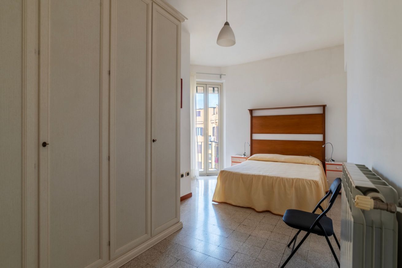 A bedroom with a bed, a chair, a wardrobe, and a radiator.
