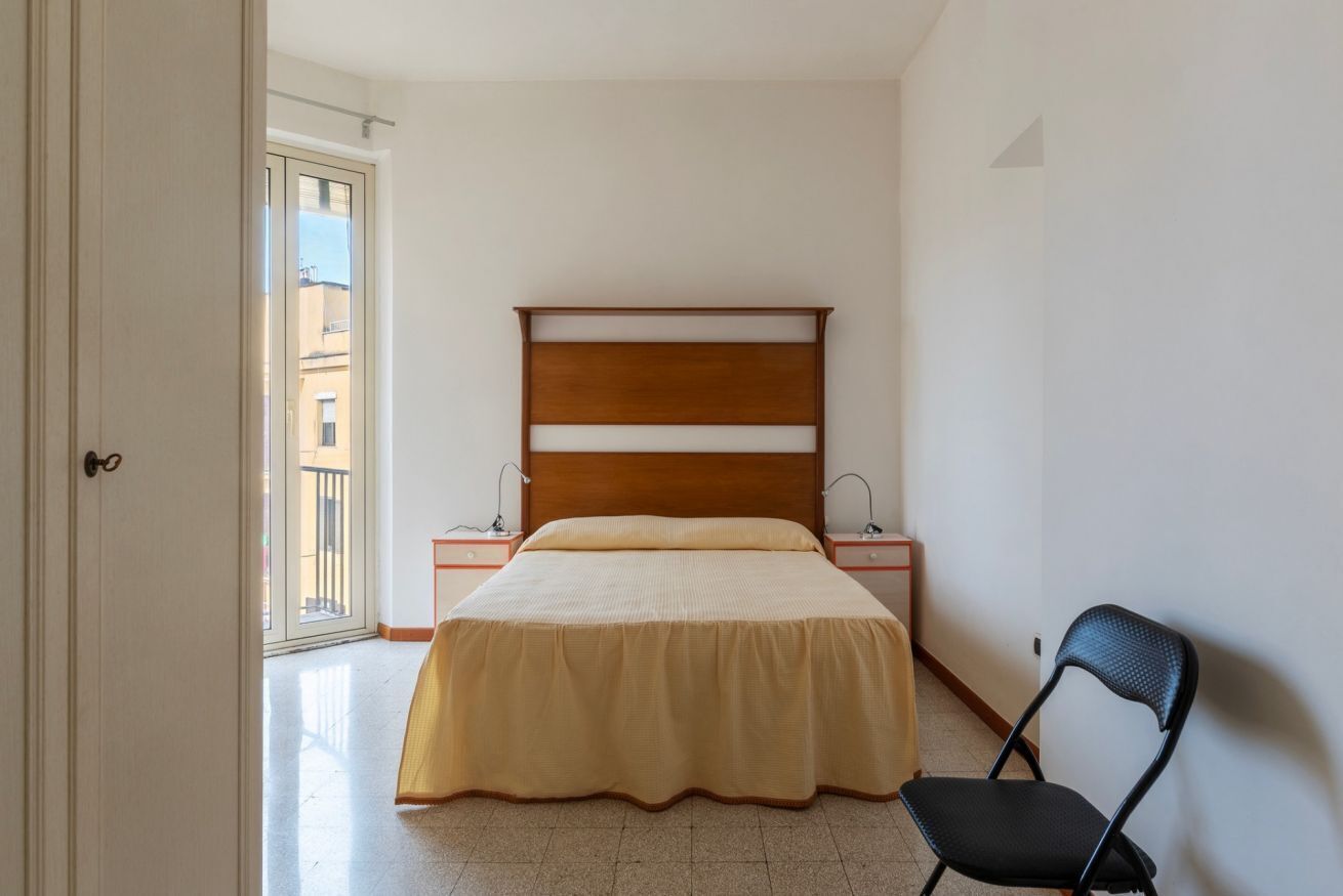 A bedroom with a bed, bedside tables, a chair, and a door leading to a balcony.