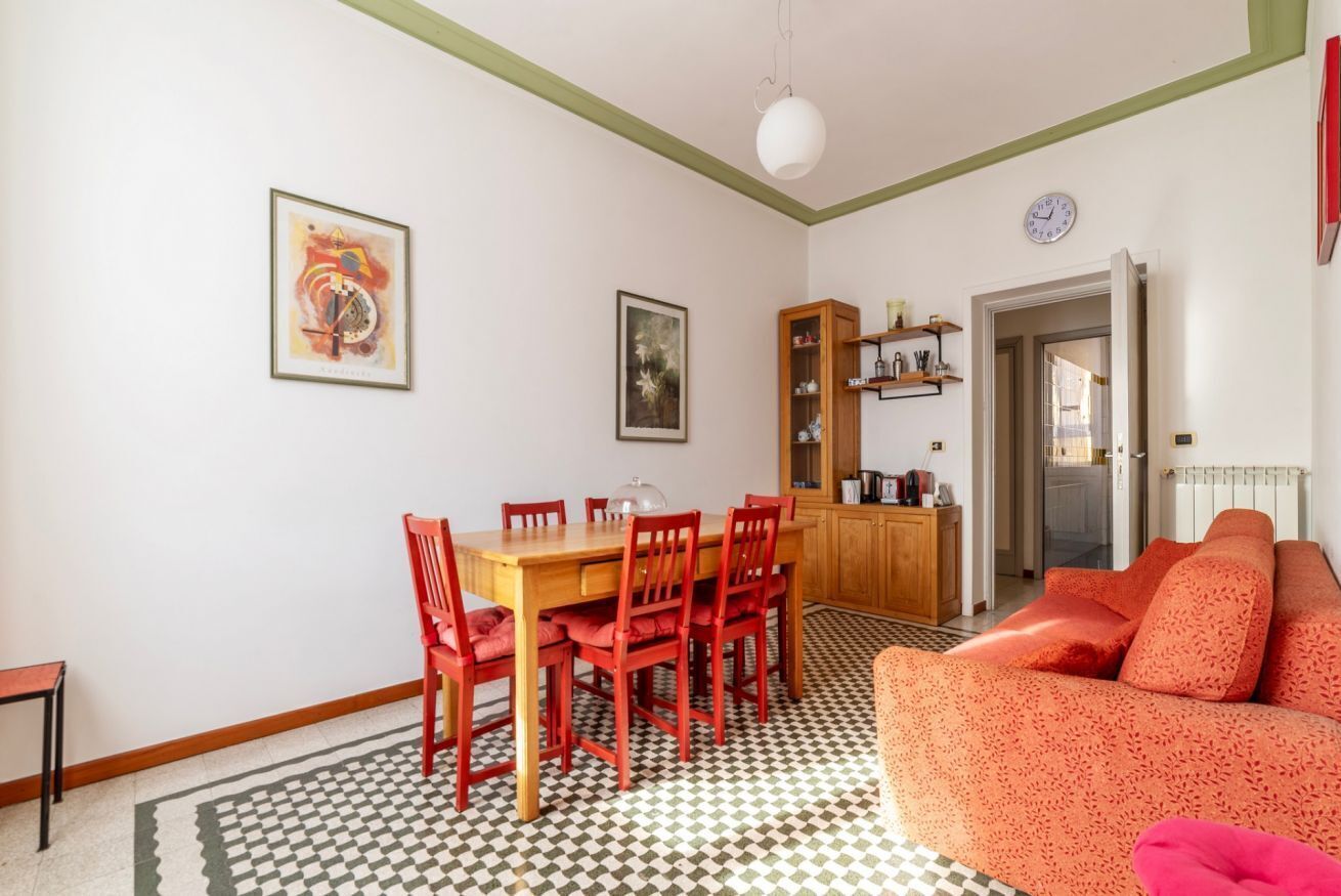 Ein Essbereich mit Holztisch, roten Stühlen, einem gemusterten Boden und einer Couch mit orangefarbenen Kissen.