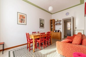 Un comedor con una mesa de madera y sillas rojas, suelo con estampado y un sofá con cojines naranja.