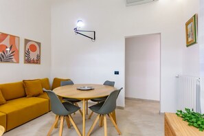 A modern living room with a round wooden table, grey chairs, a mustard-colored sofa, and abstract wall art.