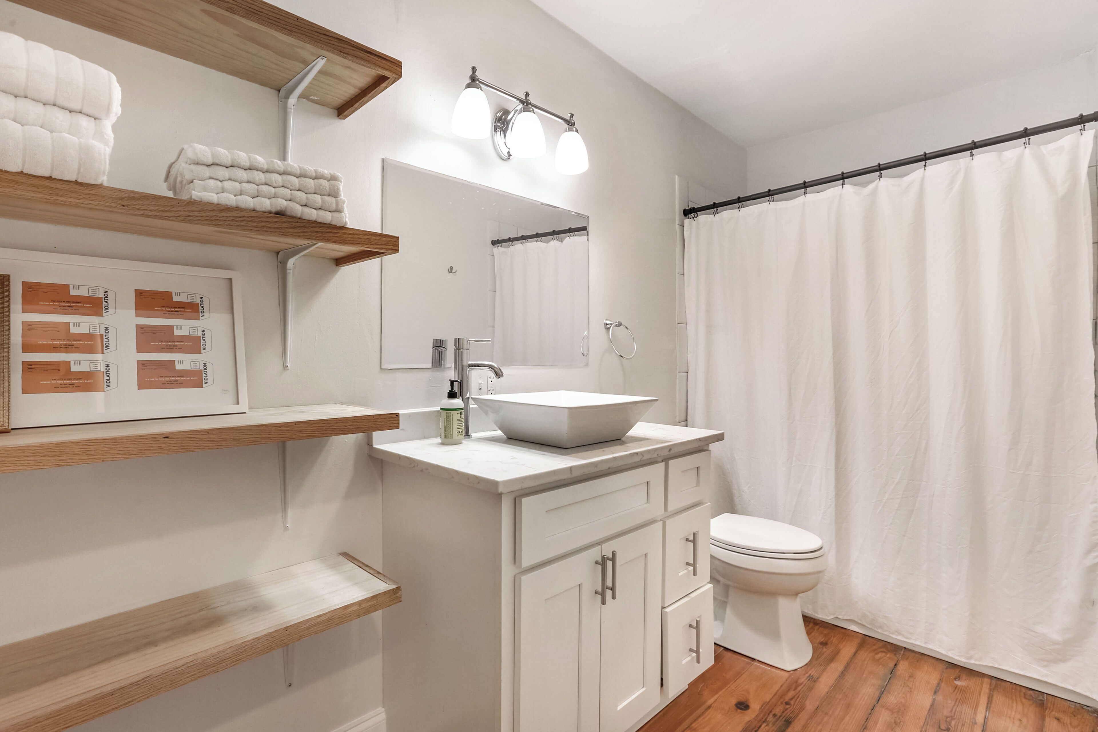 A modern bathroom with a white sink, vanity, and toilet. There are wooden shelves with towels and a shower curtain.