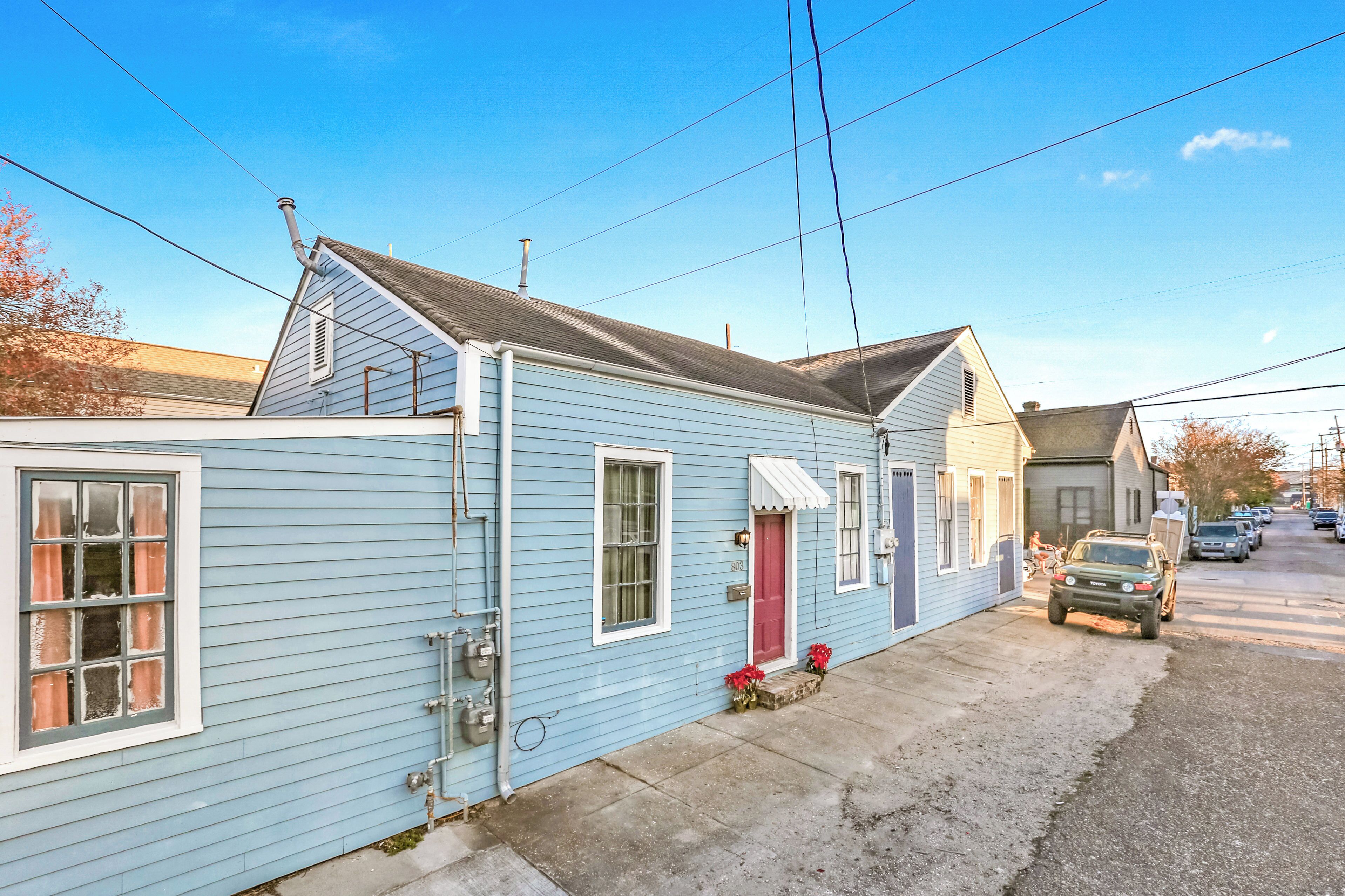 A light blue single-story house with a red door, a small front porch, and a parked vehicle on the street.