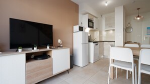 Eine moderne Küche mit Flachbildfernseher, Mikrowelle, Kühlschrank und Geschirrspüler. Ein Essbereich mit weißen Stühlen und einem Holztisch.