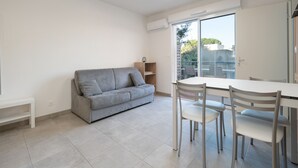 A modern living room with a grey sofa, a dining table with chairs, and a sliding glass door leading to a balcony. - Nice villa for 6 pers with garden (Sérignan)