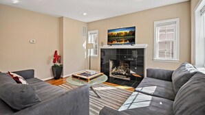 A modern living room with a fireplace, grey sofas, a coffee table, and a painting above the fireplace. - Fresh | 4 bedroom | Luxury | Center | Sunny (Falls Church)