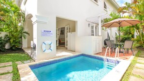 A swimming pool with a lifebuoy, a notice sign, and a patio area with a table and chairs.