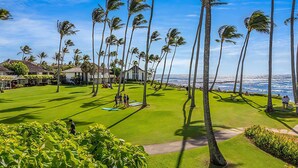 A well-maintained lawn with palm trees, a clear view of the ocean, and a building with a thatched roof. - Kiahuna Plantation Resort 116 Partial Ocean 2BD 2B (Koloa)