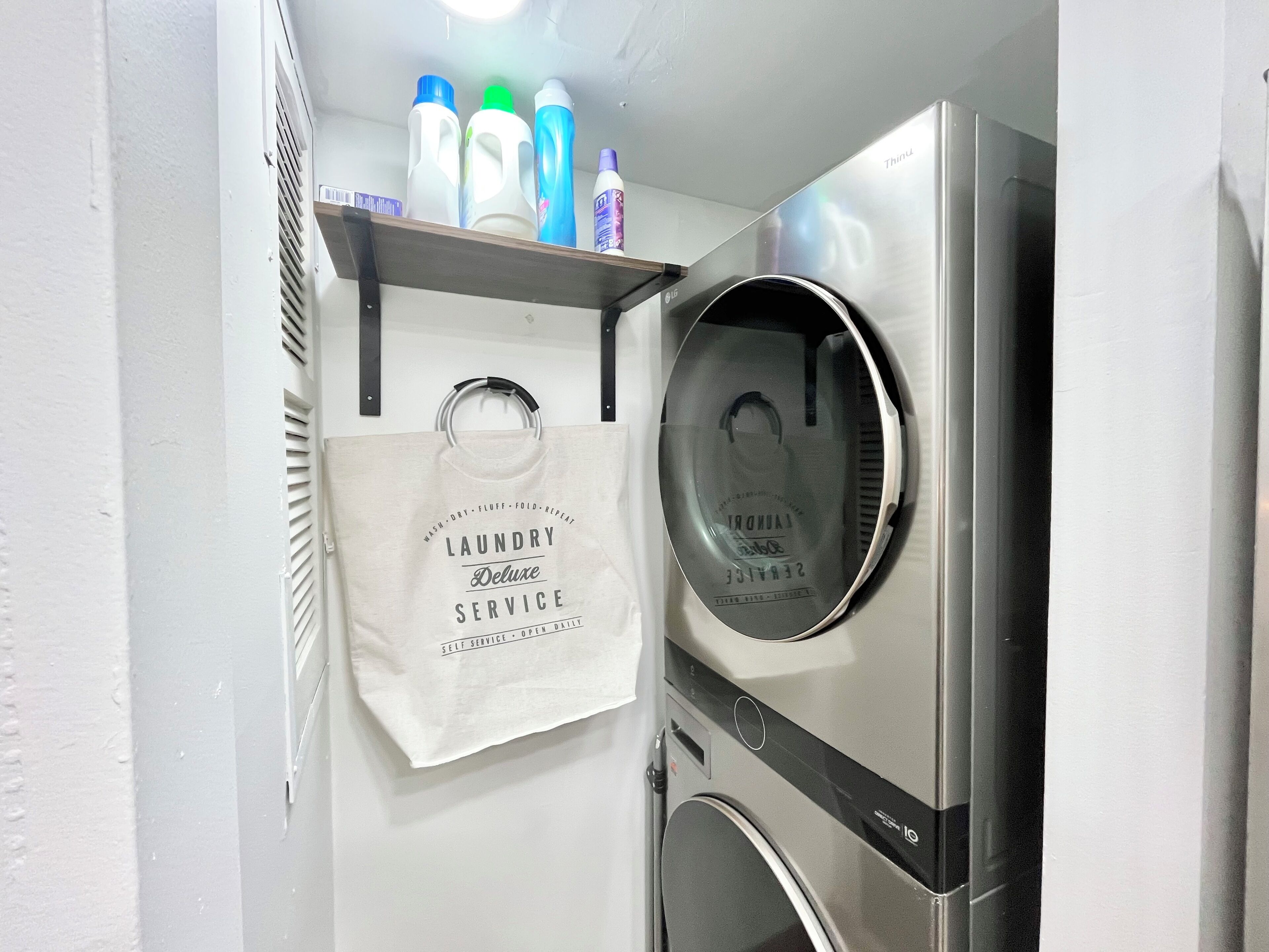 A laundry area with a self-service machine, a hanging bag, and detergent bottles.
