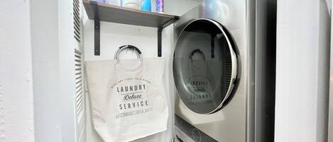 A laundry area with a self-service machine, a hanging bag, and detergent bottles.