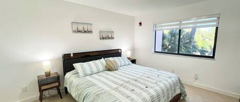 A bedroom with a bed, nightstands, a window with a view, and a ceiling light fixture.