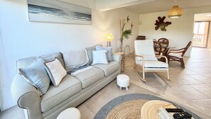 A living room with a grey sofa, white armchairs, a dining table with chairs, a hanging light fixture, and a painting on the wall. - BT 3824 Pond View Condo - Welcome to Paradise (Fort Pierce)