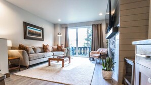 A living room with a sofa, coffee table, and a TV. There is a balcony with a railing and a plant. - Luxury in Downtown McCall, Walking Distance to Everything Downtown (McCall)