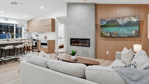Een moderne keuken met houten kastjes, een eethoek met een houten tafel, en een woonkamer met een bank en een open haard.