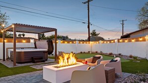 Een terras buiten met vuurkorf, zitgedeelte en een pergola met lichtjes.