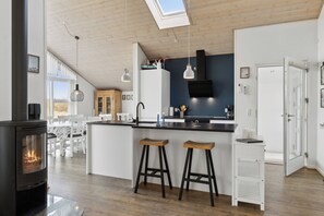 Eine moderne Küche mit einer zentralen Kochinsel, Barhocker, einem integrierten Herd, Pendelleuchten und einem großen Fenster.