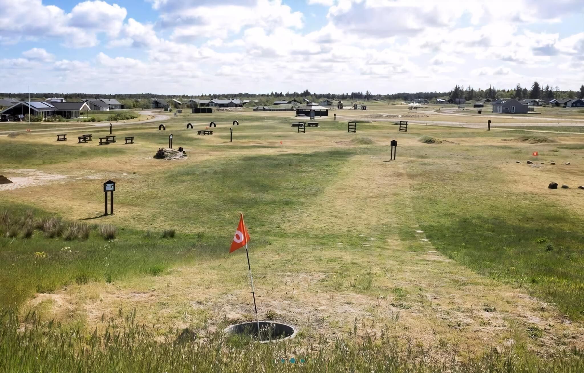 Een landelijk landschap met open velden, verspreide bankjes en een wimpelstok met een vlag.