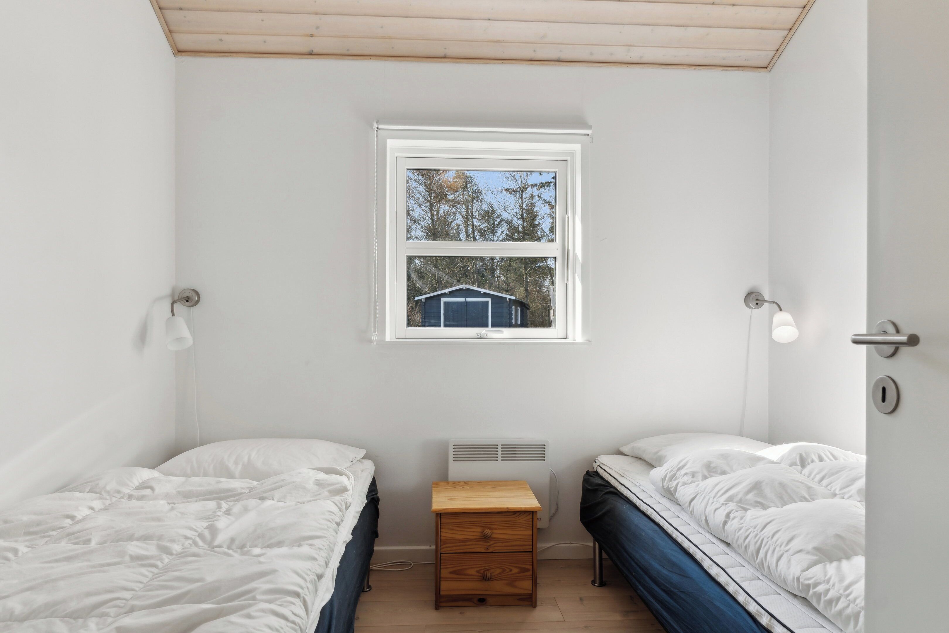 A bedroom with two beds, a window, a heater, and a nightstand.