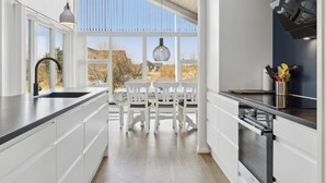 Une cuisine moderne avec des meubles blancs, une grande fenêtre et un coin repas avec des chaises blanches.