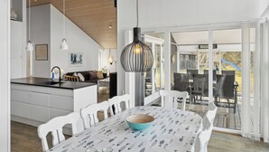 Une cuisine moderne avec des meubles blancs, un coin repas avec des chaises blanches et une grande fenêtre donnant sur une terrasse.
