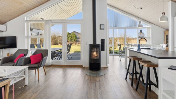 Une cuisine moderne dotée d’un poêle à bois central, d’un coin repas avec des chaises et une table, et de grandes portes-fenêtres coulissantes donnant sur un patio extérieur.