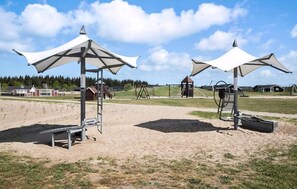 A beach with two large umbrellas, a playground, and a building in the background. - Holiday dream on the west coast (Brovst)