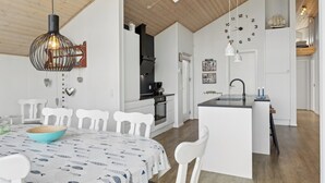 Une cuisine moderne avec des meubles blancs, un îlot central et un coin repas comprenant une table et des chaises blanches.