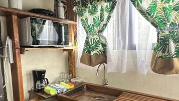 Une cuisine compacte dotée d’un plan de travail en bois, d’un évier et d’une étagère où sont rangés les ustensiles de cuisine.