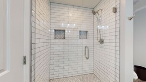 Una ducha a nivel con azulejos blancos tipo metro, un cabezal de ducha de mano y una ventana con cerramiento de vidrio.
