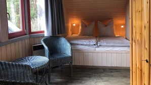 Ein gemütliches Schlafzimmer mit einem Bett, zwei Nachttischlampen, einem Korbstuhl und einem Fenster mit Vorhängen.