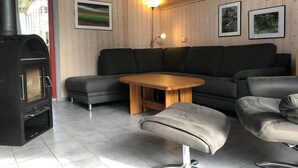 Ein modernes Wohnzimmer mit einem schwarzen Kaminofen, grauen Sofas, einem Holztisch und einem kleinen Hocker.