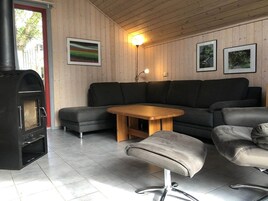 Un salon moderne avec un poêle à bois noir, des canapés gris, une table basse en bois et un petit tabouret.