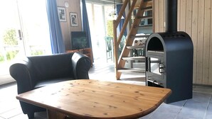 A cozy living room with a wooden table, two black armchairs, a built-in grill, and a staircase leading to an upper level.