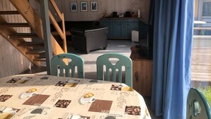 A dining area with a table covered in a coffee-themed tablecloth, two chairs, and a staircase leading to another room.
