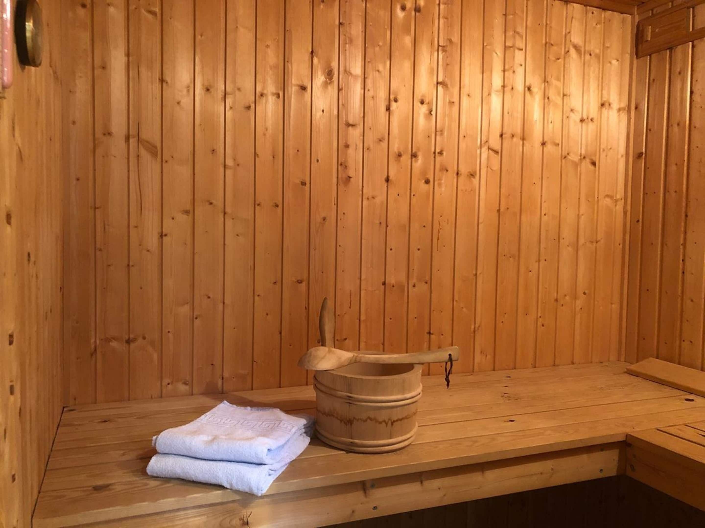 Un sauna en bois avec un banc, un seau et des serviettes.