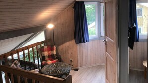 A wooden cabin interior with a balcony, a wicker chair, and a table.