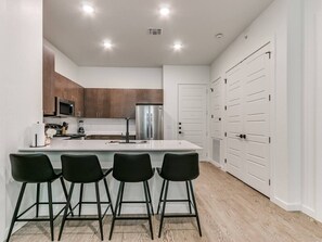 A modern kitchen with a central island, bar stools, and white cabinetry.